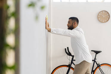 Young male entrepreneur looking at strategy while leaning on wall at office - GIOF12285