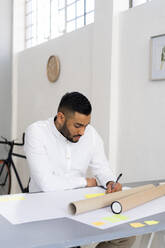 Männlicher Unternehmer, der am Schreibtisch sitzend im Büro eine Strategie plant - GIOF12290