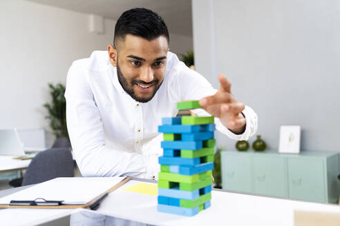 Lächelnder männlicher Unternehmer hält Spielzeugblock im Büro - GIOF12302