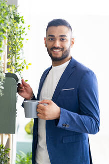Lächelnder Geschäftsmann mit Kaffeetasse in der Nähe des Briefkastens im Büro - GIOF12308