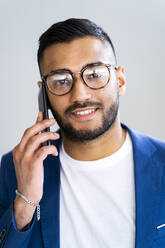 Businessman with eyeglasses talking on smart phone by wall in office - GIOF12312