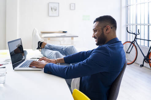 Entspannter Geschäftsmann arbeitet am Laptop in einem modernen Büro - GIOF12314