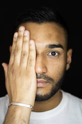 Mann bedeckt Auge mit Hand gegen schwarzen Hintergrund - GIOF12324