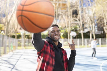 Aktiver junger Mann, der an einem sonnigen Tag Basketball spielt und gestikuliert - JCCMF01818