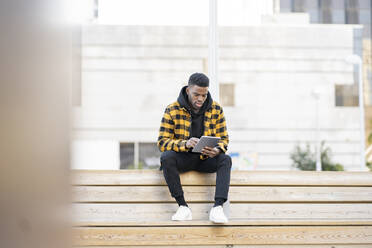 Gut aussehender junger Mann, der auf einer Holzbank sitzend ein digitales Tablet benutzt - JCCMF01828