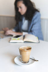 Kaffee auf dem Tisch, während eine Geschäftsfrau in einem Café arbeitet - JAQF00454