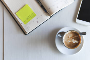 Coffee cup by mobile phone and diary on table - JAQF00455