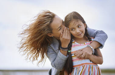 Mother whispering secret in daughter's ear - AZF00246