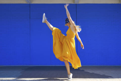 Sorglose Frau tanzt an einer blauen Wand an einem sonnigen Tag - AZF00277