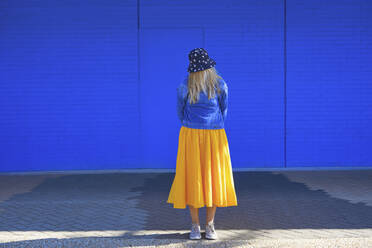 Kaukasische Frau mit Eimer Hut und Jeansjacke vor blauer Wand stehend - AZF00280