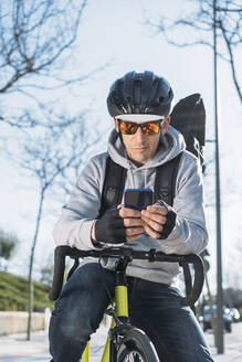 Älterer Zusteller, der sich auf ein Fahrrad stützt und ein Smartphone benutzt - DAMF00770