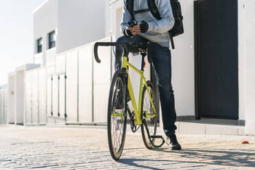 Lieferwagenfahrer mit Fahrrad auf dem Gehweg, der an einem sonnigen Tag sein Smartphone benutzt - DAMF00782