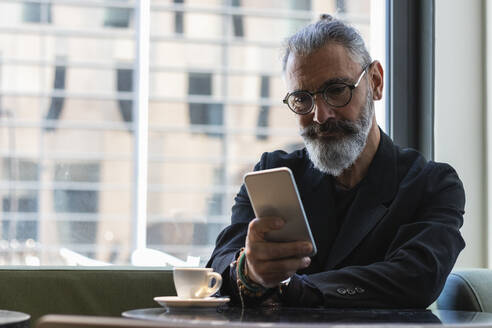 Geschäftsmann mit Brille benutzt Smartphone in einem Café - PNAF01333