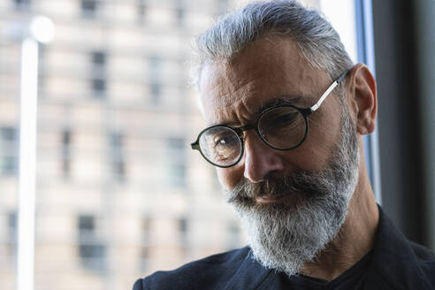 Thoughtful businessman with eyeglasses in coffee shop - PNAF01334