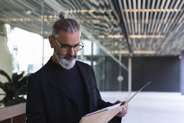 Businessman reading file in front of building - PNAF01347