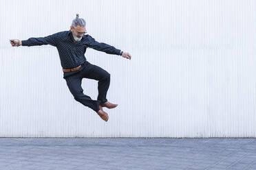 Mature man looking down while jumping on footpath - PNAF01352