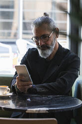 Geschäftsmann, der ein Mobiltelefon benutzt, während er in einem Cafe sitzt - PNAF01366