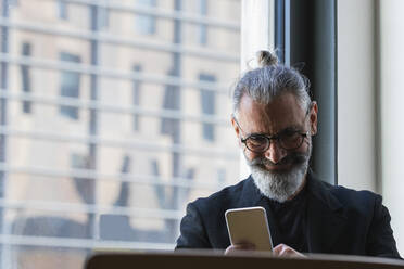 Lächelnder männlicher Unternehmer, der in einem Café an einem Mobiltelefon arbeitet - PNAF01367