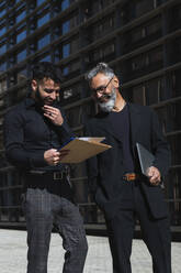 Cheerful male entrepreneurs smiling while looking at business plan in city - PNAF01372