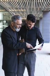 Male professionals working on business plan on walkway - PNAF01380