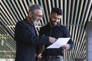 Smiling businessman explaining business plan to male colleague at entrance - PNAF01381