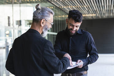 Lächelnde männliche Unternehmer, die am Eingang über einen Geschäftsplan diskutieren - PNAF01384