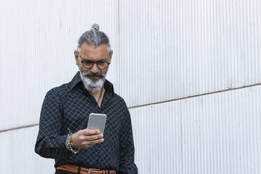 Hipster-Geschäftsmann mit Smartphone an der Wand - PNAF01385