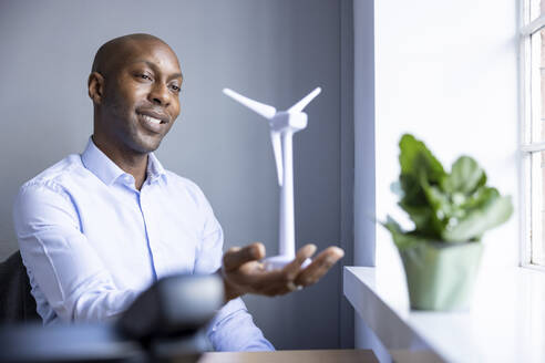 Male entrepreneur looking at wind turbine model at office - WPEF04250