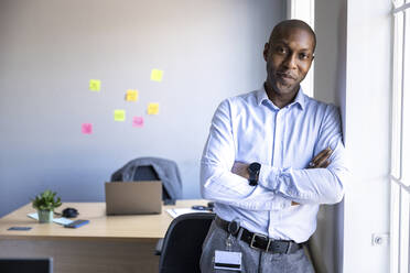 Businessman with arms crossed leaning on wall at office - WPEF04263