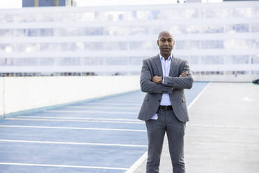 Confident businessman in suit standing at terrace parking - WPEF04267