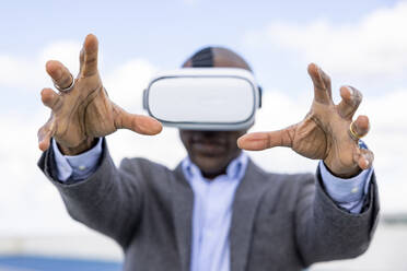 Männlicher Unternehmer gestikuliert beim Tragen eines Virtual-Reality-Headsets im Freien - WPEF04269