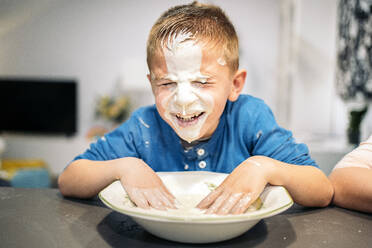 Lächelnder Junge, der sich zu Hause das Gesicht mit Mehl und Wasser einschmiert - AMPF00203