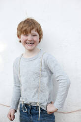 Lächelnder rothaariger Junge steht vor einer Wand im Freien - GISF00790