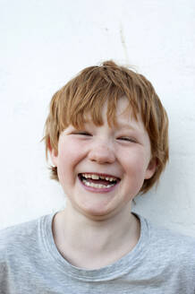 Cheerful redhead boy in front of wall outdoors - GISF00794