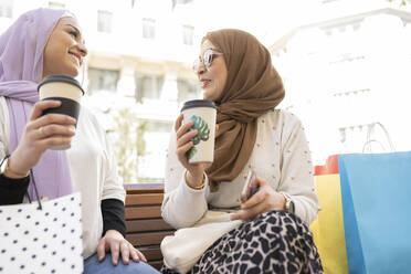 Arabische Freundinnen trinken Kaffee und sitzen auf einer Bank - JCCMF01868