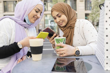 Freundinnen mit wiederverwendbaren Bechern auf dem Tisch und einem Smartphone in einem Straßencafé in der Stadt - JCCMF01871