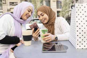 Arabische Frauen mit Kaffeetasse und Smartphone in einem Straßencafé in der Stadt - JCCMF01872
