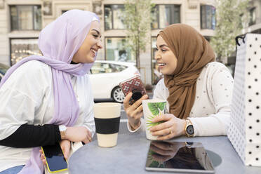 Glückliche Freundinnen mit wiederverwendbarem Becher und Smartphone in einem Straßencafé in der Stadt - JCCMF01873