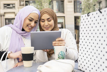 Lächelnde arabische Frauen benutzen ein digitales Tablet in einem Straßencafé in der Stadt - JCCMF01875