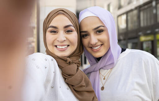 Lächelnde arabische Freundinnen in Hidschabs machen ein Selfie in der Stadt - JCCMF01885