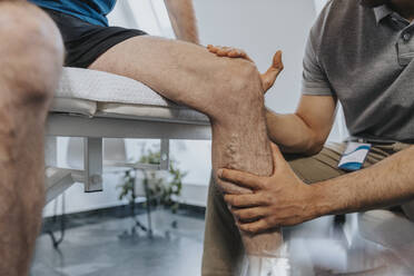 Physiotherapeutin berührt das Knie eines männlichen Patienten in der Praxis - MFF07683