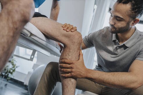 Male Physical therapist examining knee of patient in practice - MFF07684