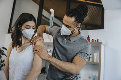 Male physiotherapist working on shoulder of female patient in practice during COVID-19 - MFF07693