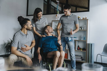 Smiling male patient looking at physical therapist gesturing by colleagues in practice - MFF07715