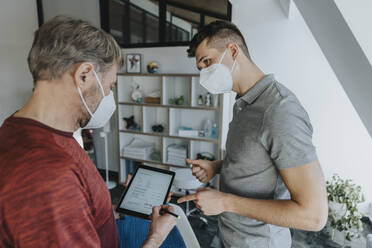 Male physiotherapist gesturing while patient signing digital form during pandemic - MFF07774