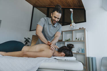 Smiling physiotherapist giving spine and upper back massage to female patient in medical practice - MFF07816