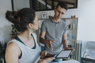 Male physiotherapist with digital tablet discussion with female patient in medical practice - MFF07820