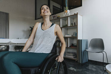 Lächelnde Patientin im Rollstuhl sitzend und wegschauend in einer Arztpraxis - MFF07836