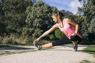 Mid adult woman stretching on footpath in forest during sunny day - ABZF03525