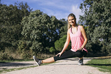 Smiling woman stretching in forest during sunny day - ABZF03526